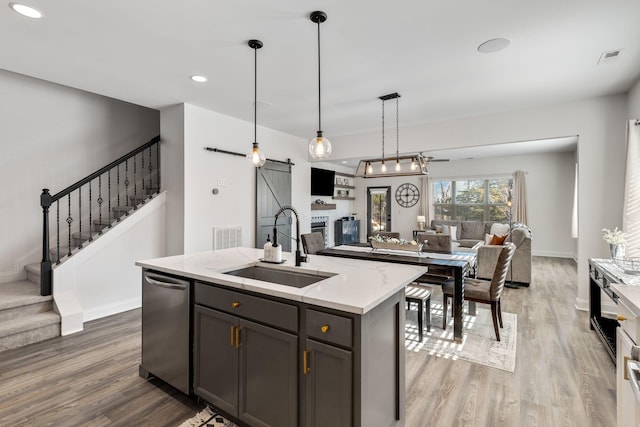 kitchen featuring sink, light stone countertops, a center island with sink, decorative light fixtures, and a barn door