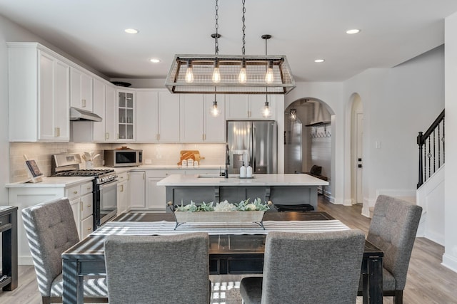 kitchen with appliances with stainless steel finishes, a kitchen island with sink, backsplash, white cabinetry, and decorative light fixtures