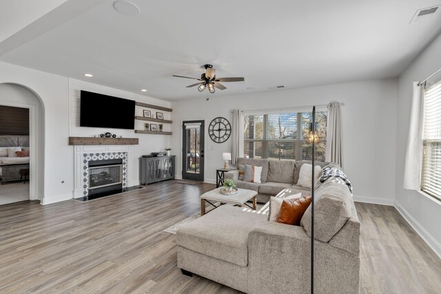 living room with light hardwood / wood-style flooring, a tile fireplace, and ceiling fan