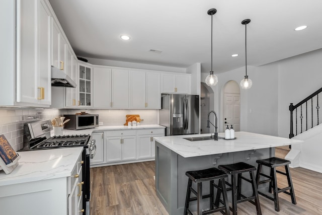 kitchen featuring hanging light fixtures, stainless steel appliances, light stone countertops, an island with sink, and white cabinets