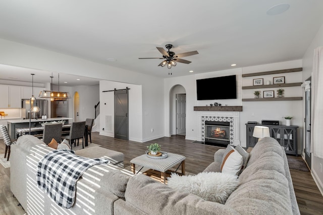 living room featuring a tile fireplace, a barn door, hardwood / wood-style floors, and ceiling fan