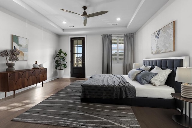 bedroom with ceiling fan, access to exterior, a tray ceiling, and dark hardwood / wood-style flooring