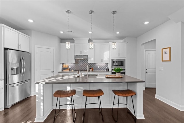 kitchen with decorative light fixtures, backsplash, a kitchen island with sink, appliances with stainless steel finishes, and white cabinets