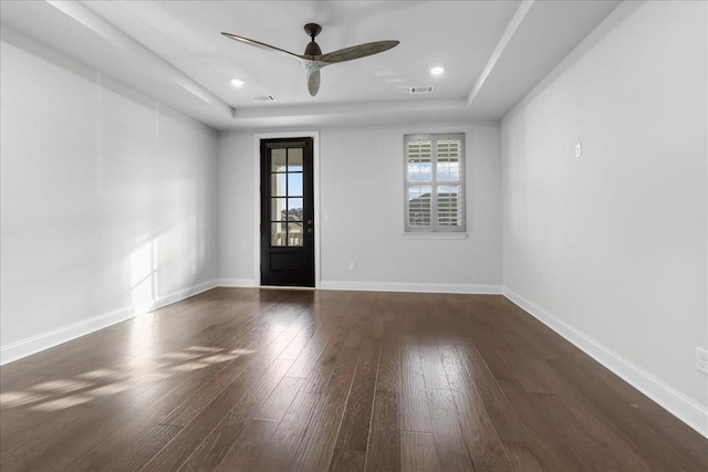 empty room with ceiling fan, a raised ceiling, and dark hardwood / wood-style floors