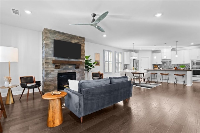 living room featuring dark wood-type flooring, a stone fireplace, and ceiling fan