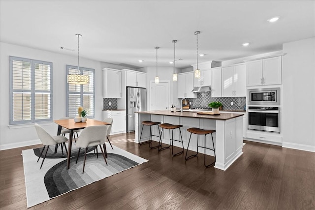 kitchen featuring white cabinetry, stainless steel appliances, a center island with sink, and hanging light fixtures