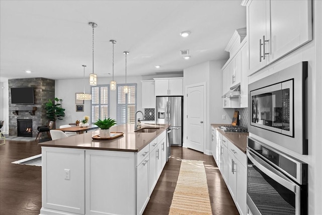 kitchen with sink, white cabinetry, hanging light fixtures, a kitchen island with sink, and appliances with stainless steel finishes