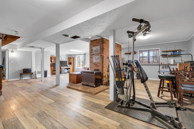 workout room with light hardwood / wood-style floors, a textured ceiling, brick wall, and crown molding