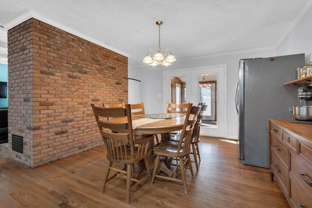 dining room with brick wall, dark hardwood / wood-style floors, crown molding, and a notable chandelier