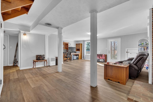 interior space featuring a textured ceiling, light wood-type flooring, and decorative columns