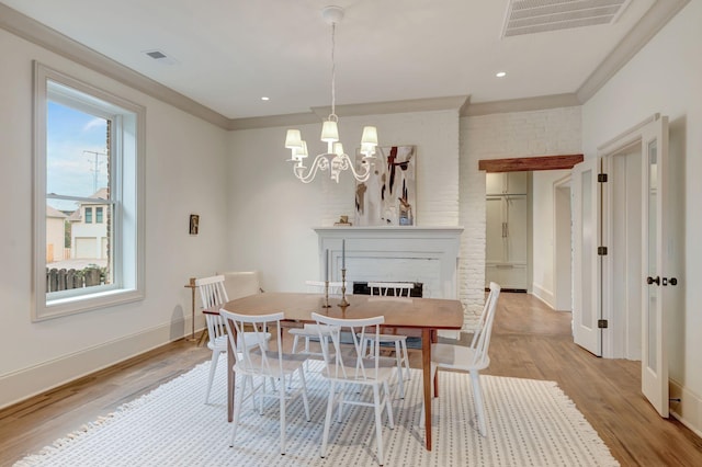 dining area featuring a notable chandelier, crown molding, a fireplace, and light hardwood / wood-style floors