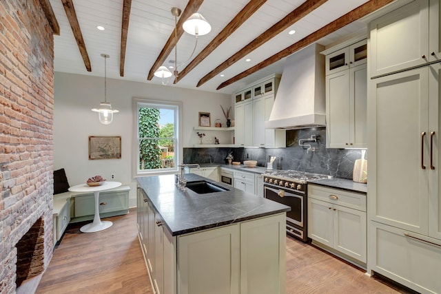 kitchen with sink, premium range hood, a kitchen island with sink, gas range oven, and decorative light fixtures