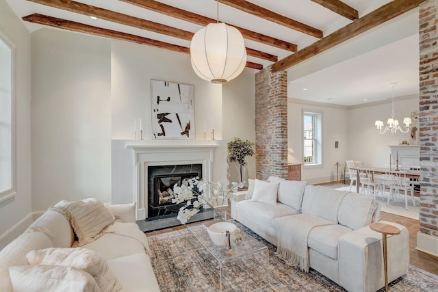 living room featuring beamed ceiling, a premium fireplace, hardwood / wood-style floors, and an inviting chandelier