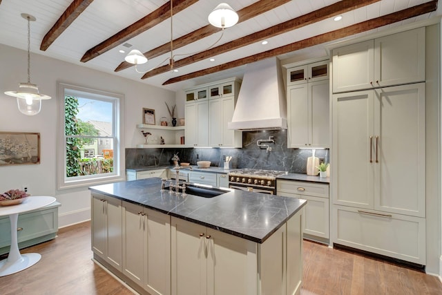 kitchen featuring sink, premium range hood, a kitchen island with sink, stainless steel range, and decorative backsplash