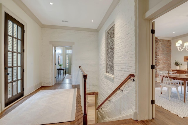 hall with an inviting chandelier, brick wall, and wood-type flooring