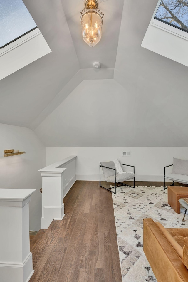 additional living space with an inviting chandelier, wood-type flooring, and lofted ceiling with skylight