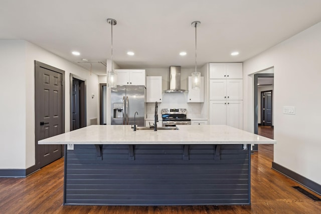 kitchen featuring wall chimney range hood, pendant lighting, a center island with sink, white cabinetry, and stainless steel appliances