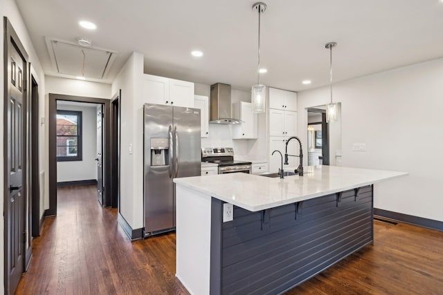 kitchen with pendant lighting, a kitchen island with sink, appliances with stainless steel finishes, white cabinets, and wall chimney exhaust hood