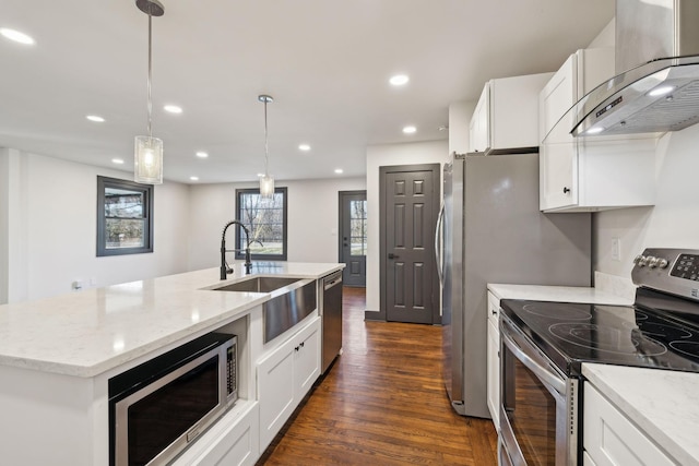 kitchen with exhaust hood, white cabinetry, appliances with stainless steel finishes, decorative light fixtures, and a kitchen island with sink