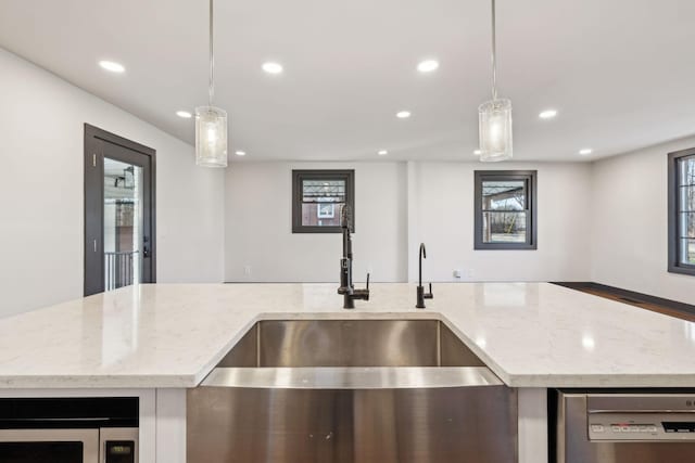 kitchen featuring sink, hanging light fixtures, light stone counters, stainless steel dishwasher, and a center island with sink