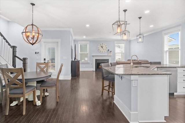 kitchen with hanging light fixtures, sink, white cabinets, a breakfast bar, and stone counters