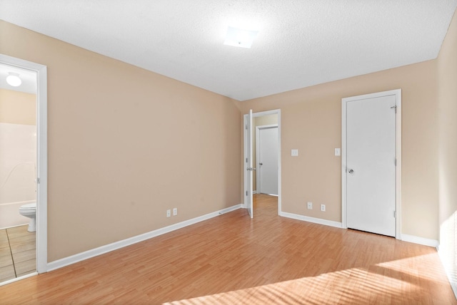 unfurnished bedroom with ensuite bathroom, a textured ceiling, and light hardwood / wood-style flooring