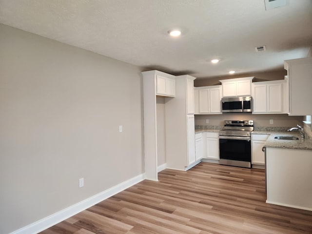 kitchen featuring white cabinetry, light hardwood / wood-style floors, stainless steel appliances, light stone countertops, and sink