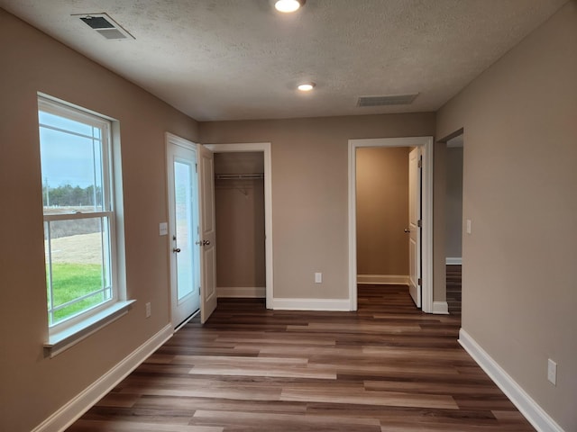 unfurnished bedroom with multiple windows, dark hardwood / wood-style floors, a closet, and a textured ceiling