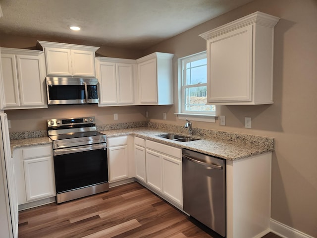 kitchen with stainless steel appliances, white cabinetry, light stone counters, and sink