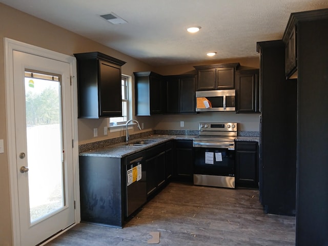 kitchen with appliances with stainless steel finishes, a wealth of natural light, dark wood-type flooring, and a sink