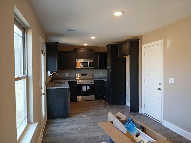 kitchen with stainless steel appliances, a sink, visible vents, baseboards, and dark wood finished floors