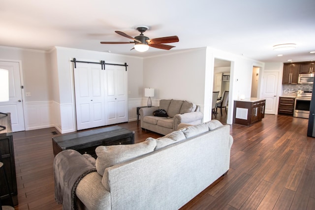 living room featuring ceiling fan, a barn door, dark hardwood / wood-style flooring, and ornamental molding