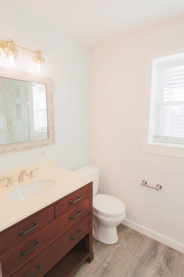 bathroom with a wealth of natural light, toilet, vanity, and hardwood / wood-style floors