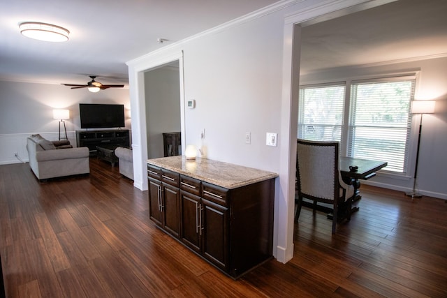 kitchen with dark brown cabinetry, dark wood-type flooring, ceiling fan, ornamental molding, and light stone counters