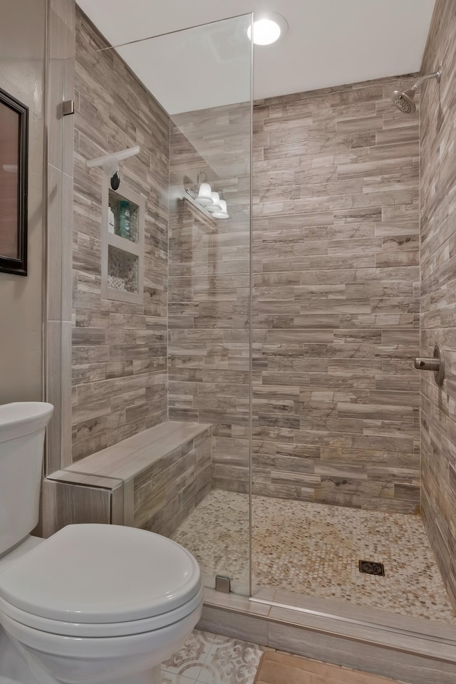 bathroom featuring toilet, tile patterned flooring, and a tile shower