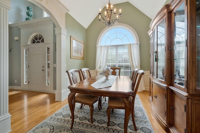 dining room with high vaulted ceiling, decorative columns, a chandelier, and light wood-type flooring