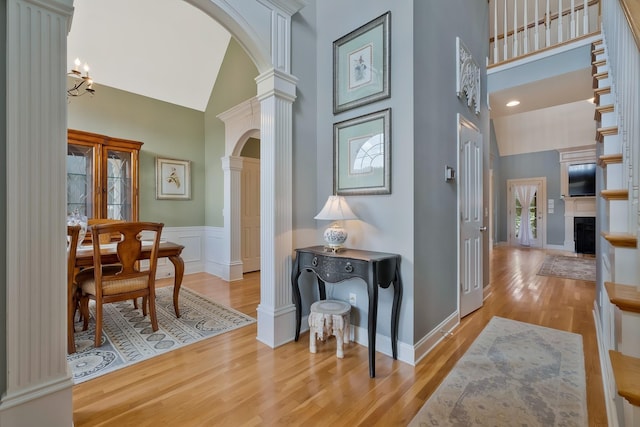 corridor with light hardwood / wood-style floors, high vaulted ceiling, and decorative columns