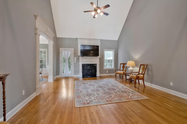 living area with high vaulted ceiling, ceiling fan, ornate columns, and light hardwood / wood-style flooring