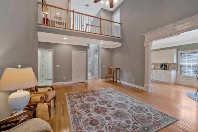 living room featuring ornate columns, light hardwood / wood-style flooring, a high ceiling, and ceiling fan