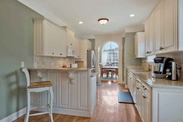 kitchen featuring backsplash, light hardwood / wood-style floors, sink, a kitchen breakfast bar, and decorative columns