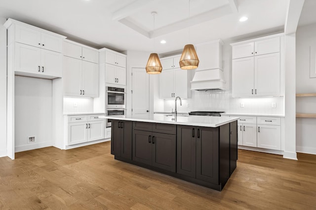 kitchen featuring pendant lighting, white cabinetry, double oven, a kitchen island with sink, and light hardwood / wood-style flooring