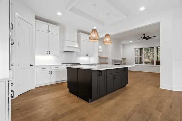 kitchen with custom exhaust hood, white cabinets, pendant lighting, and a center island with sink