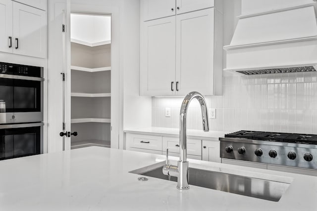 kitchen featuring decorative backsplash, white cabinetry, custom range hood, and stainless steel double oven