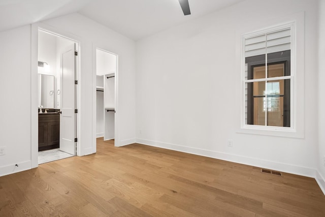 unfurnished bedroom featuring ceiling fan, ensuite bath, light wood-type flooring, a walk in closet, and a closet