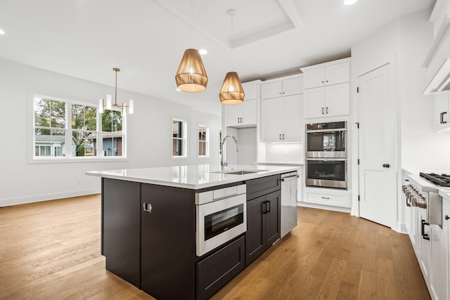 kitchen featuring a center island with sink, stainless steel appliances, a raised ceiling, hanging light fixtures, and sink