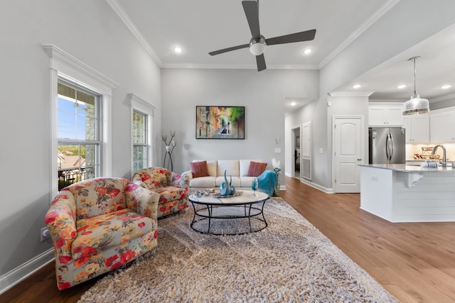 living room featuring ceiling fan, sink, ornamental molding, and light hardwood / wood-style floors