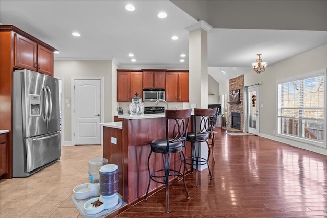 kitchen with a fireplace, an island with sink, a breakfast bar area, stainless steel appliances, and light hardwood / wood-style flooring