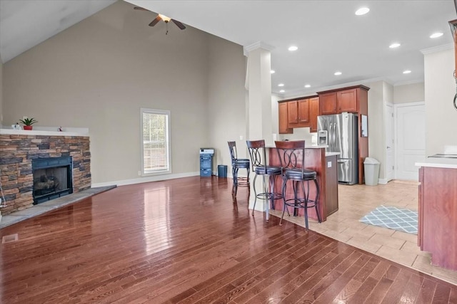 living room with crown molding, wood-type flooring, high vaulted ceiling, ceiling fan, and a fireplace