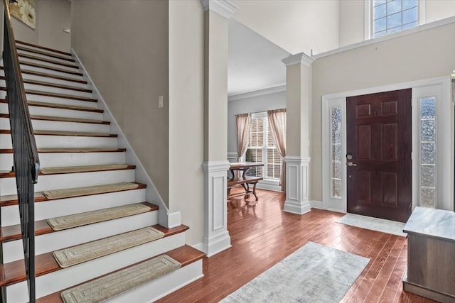 foyer featuring ornate columns, wood-type flooring, ornamental molding, and a towering ceiling