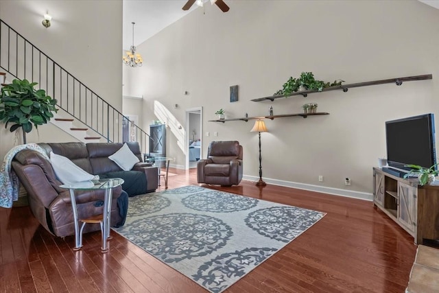 living room with dark hardwood / wood-style flooring, ceiling fan with notable chandelier, and a high ceiling